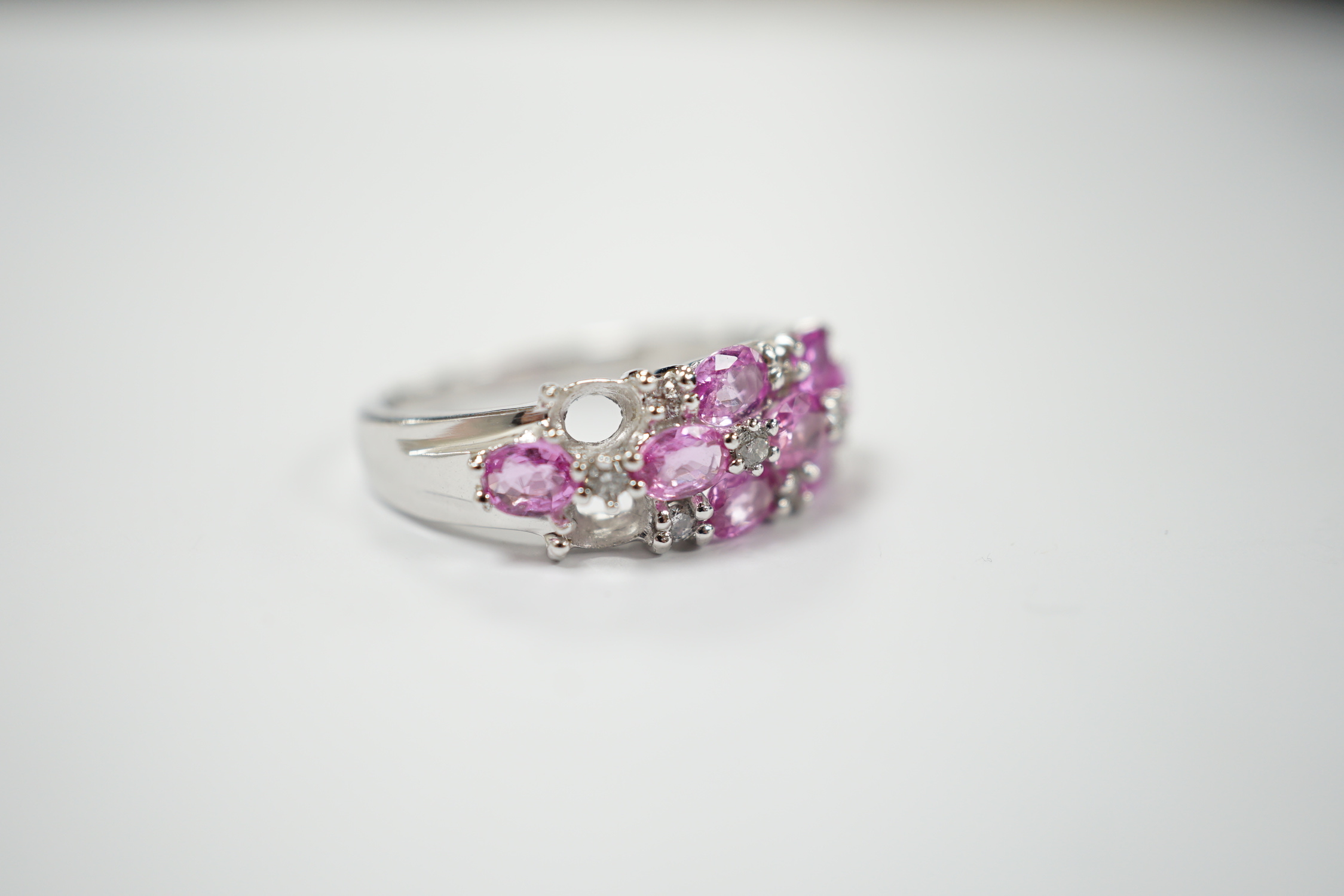 A modern 14k white metal, pink sapphire and diamond cluster set half hoop ring (two sapphires loose), size O, gross weight 4.7 grams.